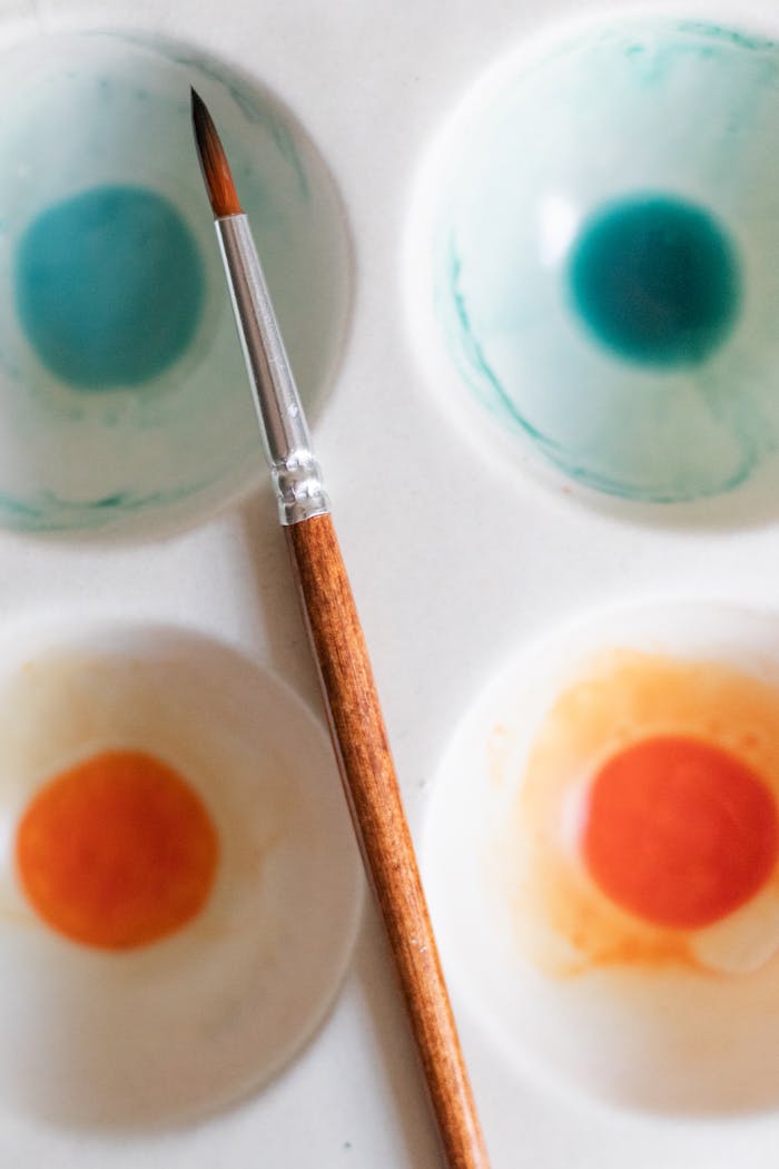 Top view of a watercolor palette with a paintbrush on textured paper.